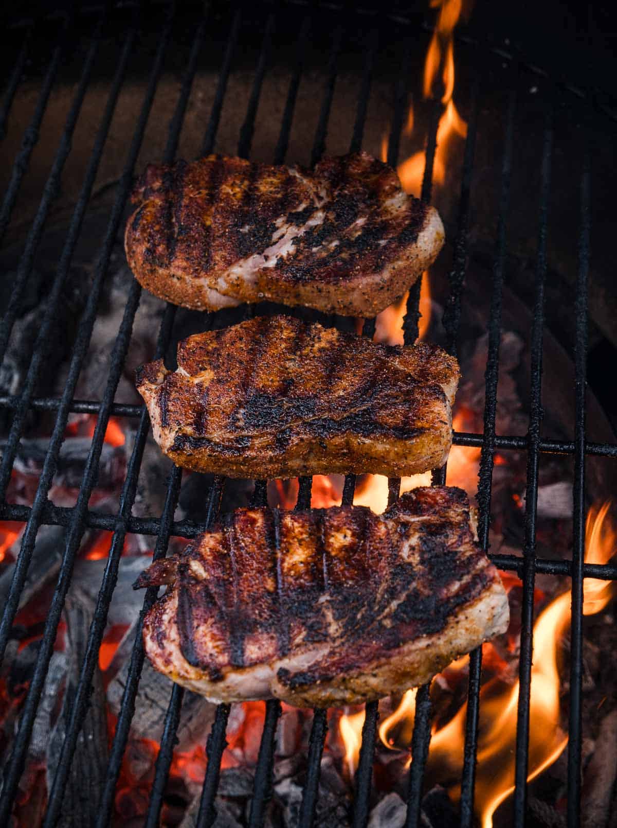 three pork chops on a hot grill with flames
