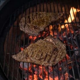 Two thin ribeye steaks grilling over a hot grill