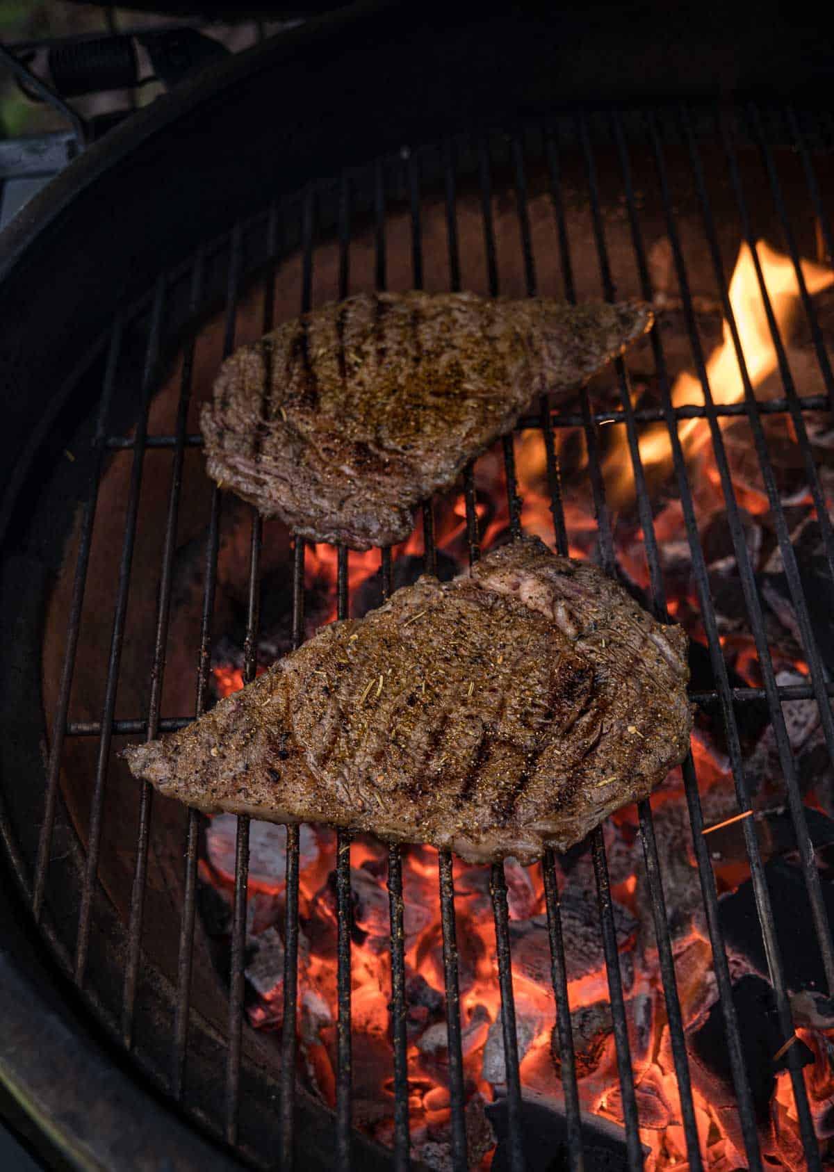 two thin steaks grilling over a hot grill