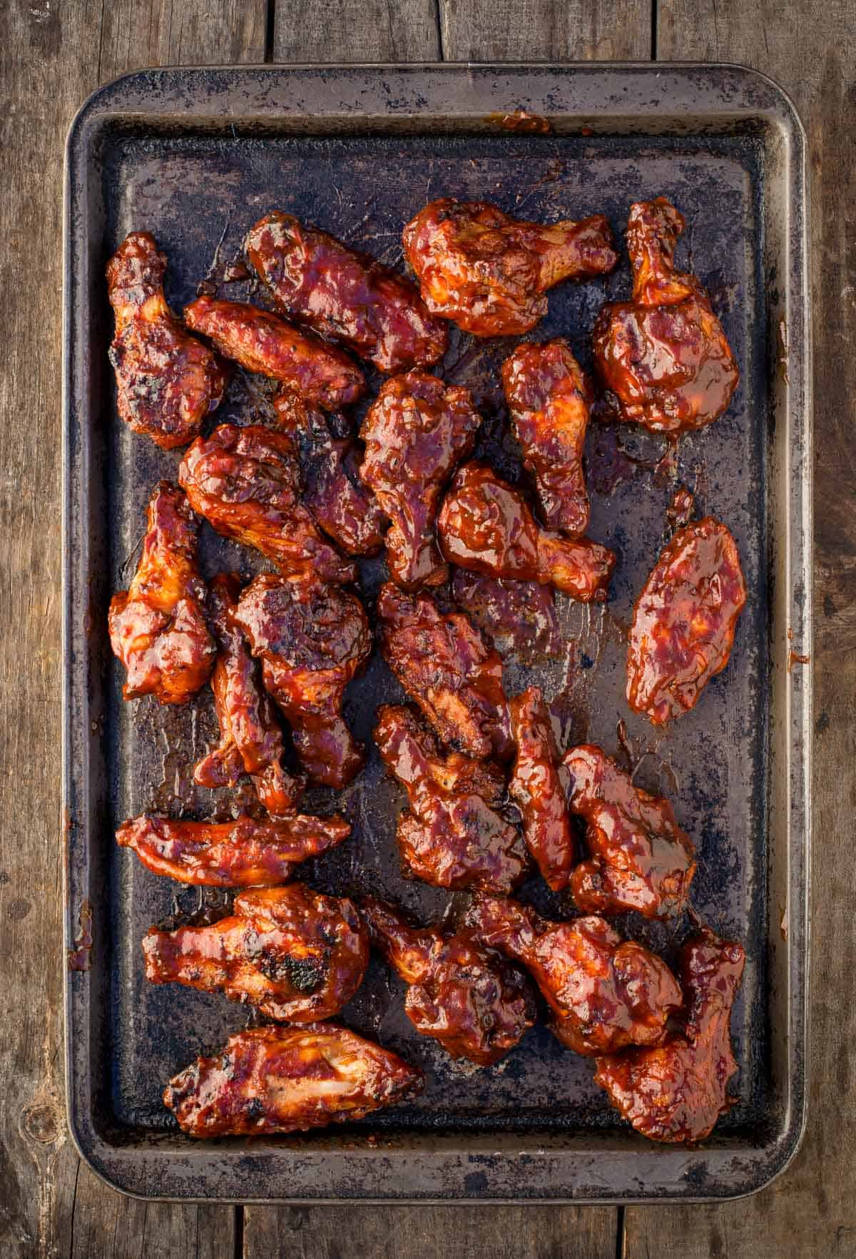 Crispy grilled chicken wings on a sheet pan with BBQ sauce