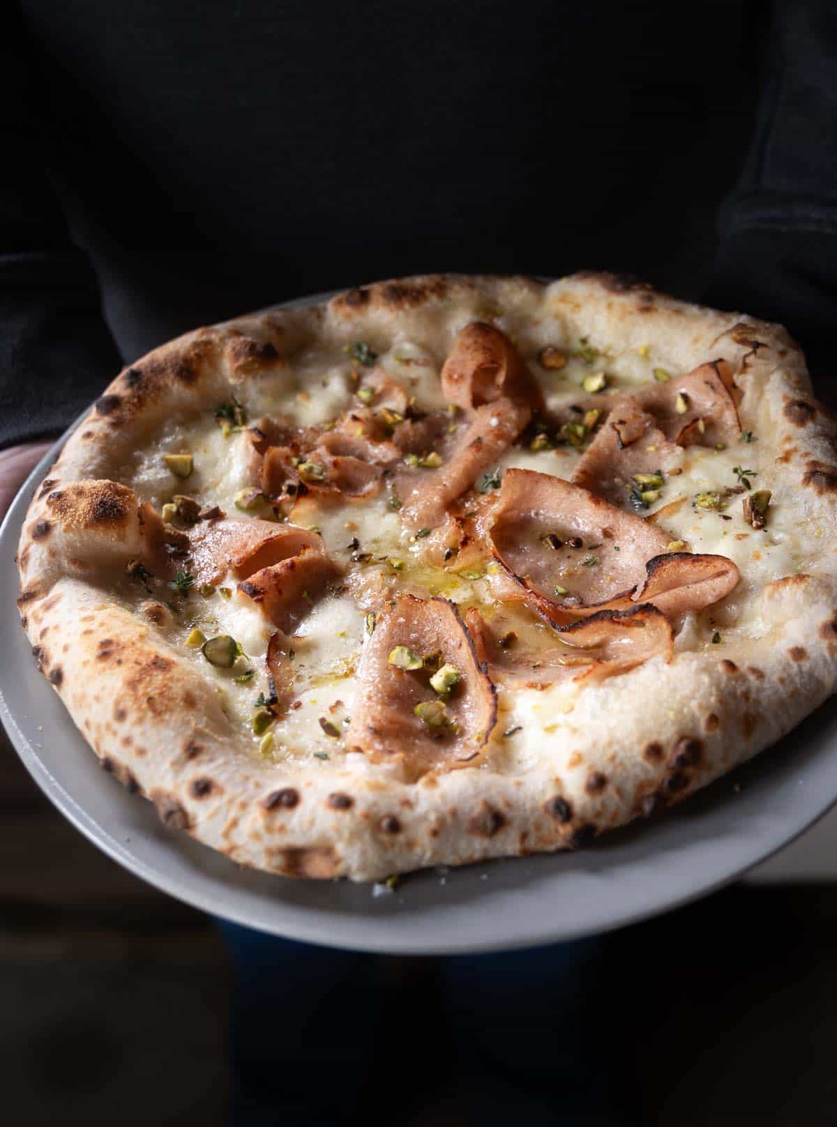 Mortadella pizza topped with pistachios on a serving platter