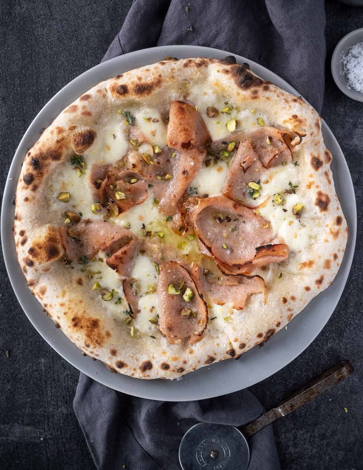 Mortadella pizza topped with pistachios on a serving platter
