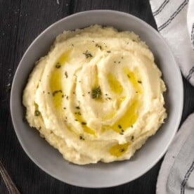 Parsnip puree in a bowl topped with melted butter and thyme.