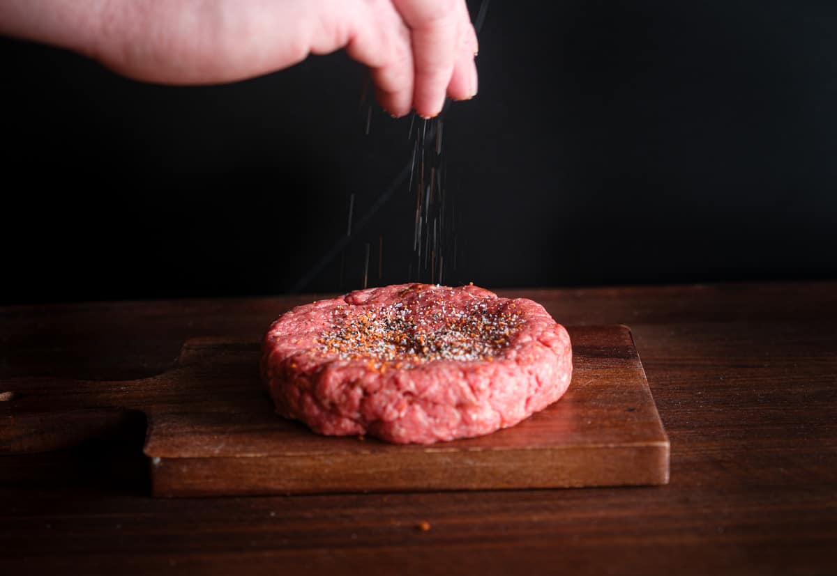 Seasoning the top of a hamburger patty ready for the smoker.