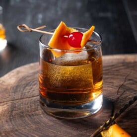 A smoked old fashioned cocktail with bourbon, smoked ice, and garnished with a cherry and orange peel in a rocks glass
