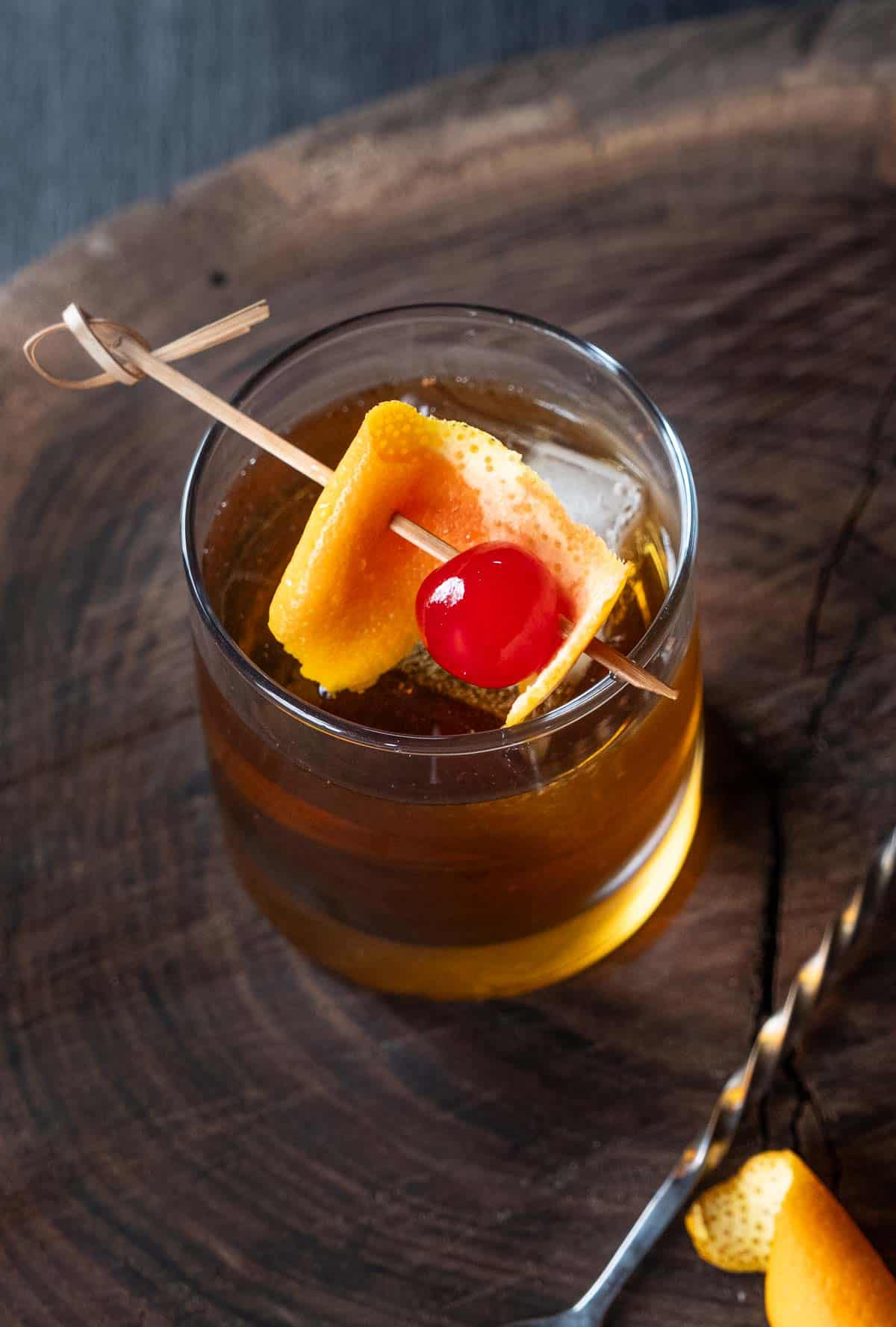 A smoked old fashioned cocktail garnished with a cocktail cherry and slice of orange in a rocks glass