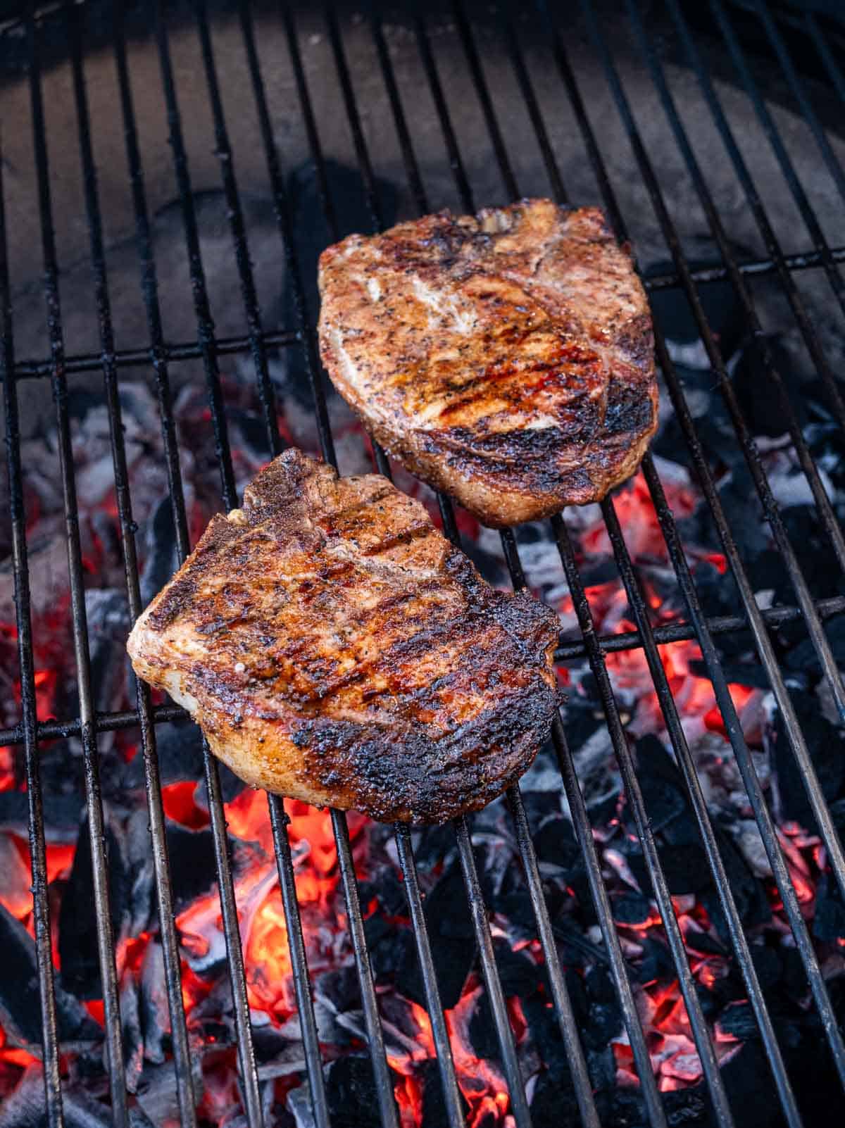 Two pork steaks cooking over a hot grill