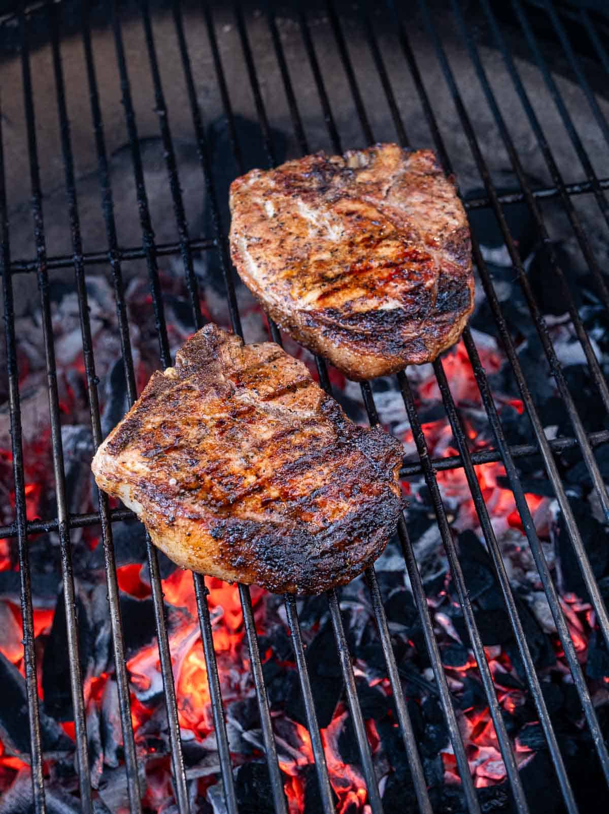 Two pork steaks cooking over a hot grill.