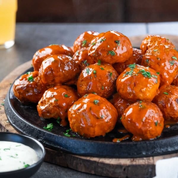 Smoked Buffalo chicken meatballs sauced and stacked on a cast iron tray with a side of ranch.