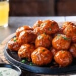 Smoked Buffalo chicken meatballs sauced and on a cast iron pan with a beer and ranch.