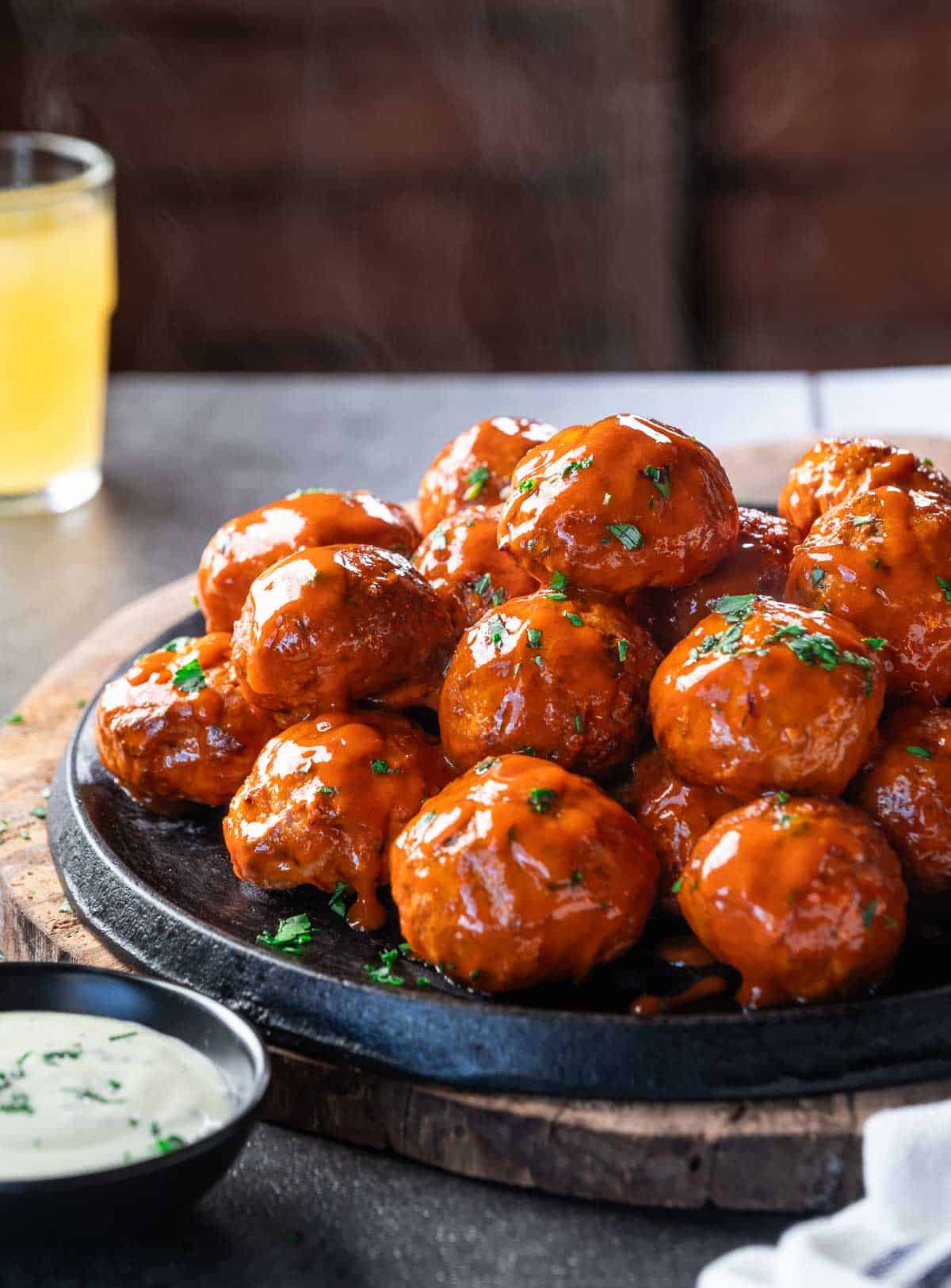 Smoked Buffalo chicken meatballs sauced and on a cast iron pan with a beer and ranch.