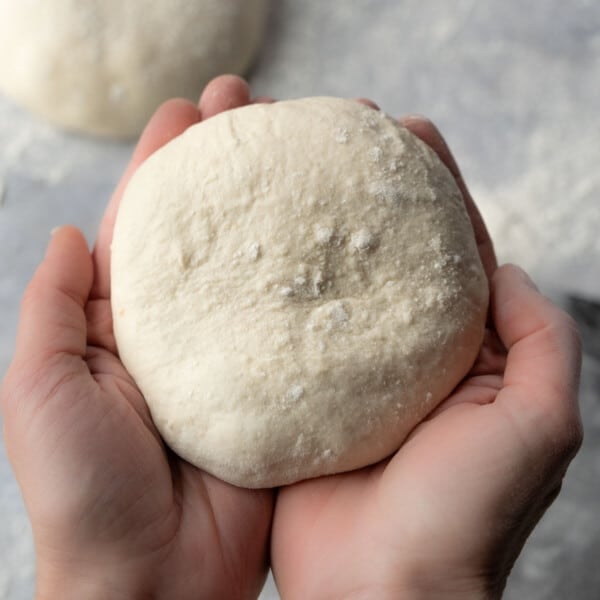 Sourdough pizza dough cupped inside of two hands
