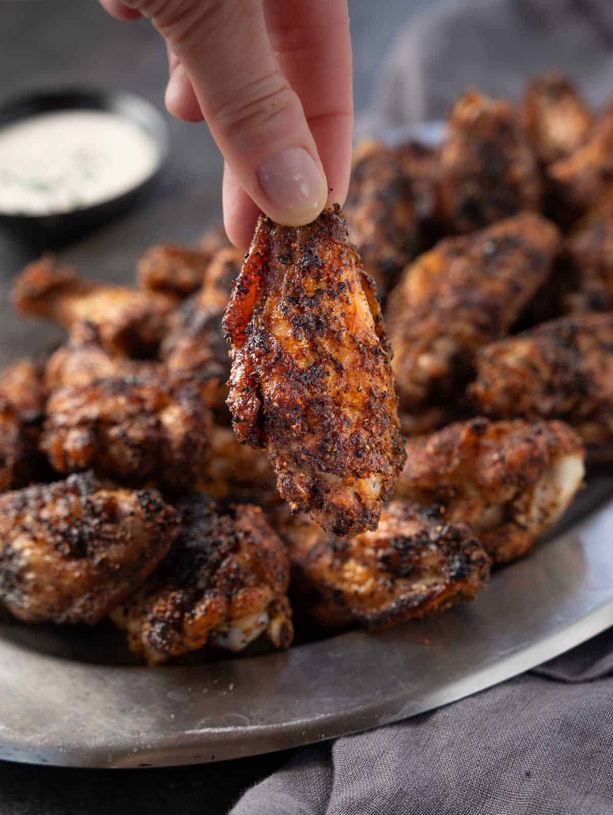 A hand holding a crispy dry rub chicken wing