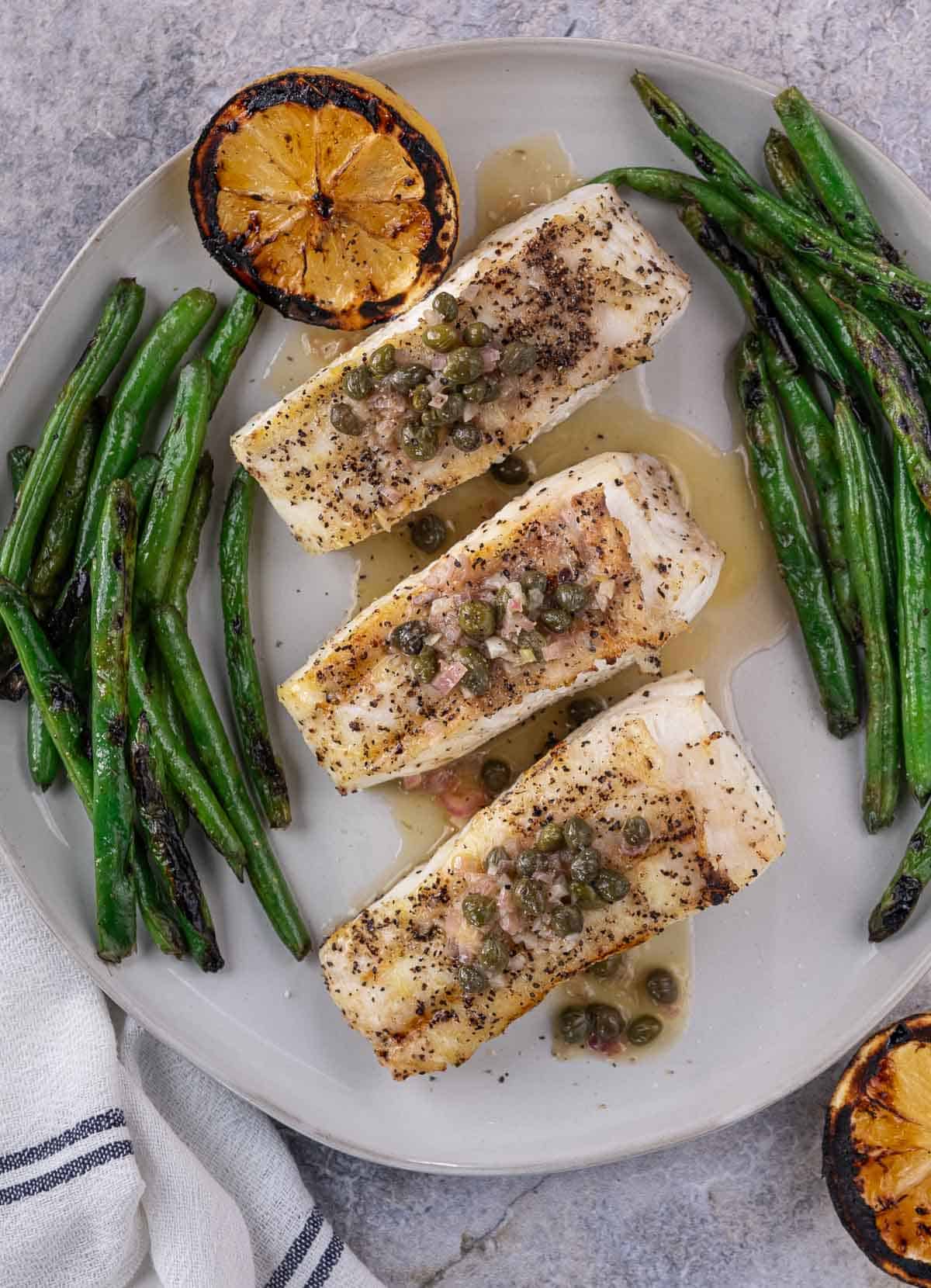 3 Slices of grilled halibut on a platter with sides of grilled green beans.
