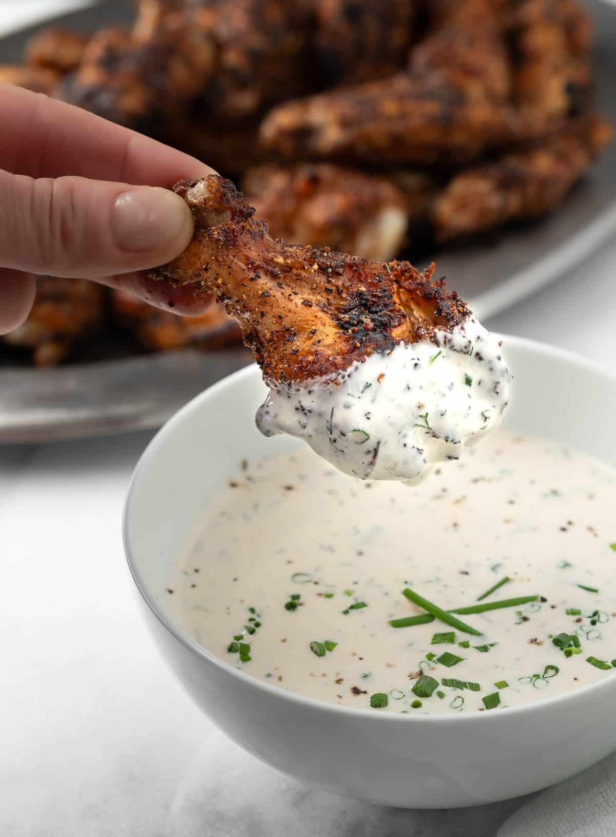 A dry rub chicken wing dunked into a bowl of homemade ranch dressing