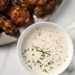 A bowl of homemade ranch dressing with some dry rub chicken wings on the side