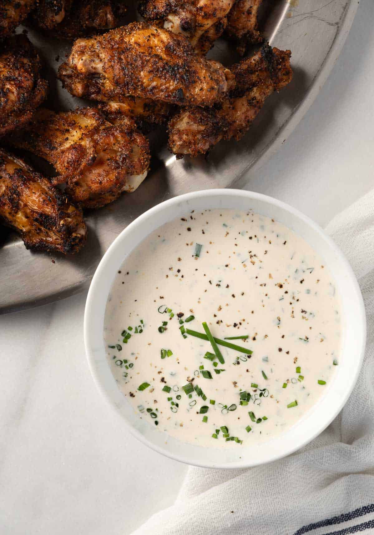 A bowl of homemade ranch dressing with some dry rub chicken wings on the side