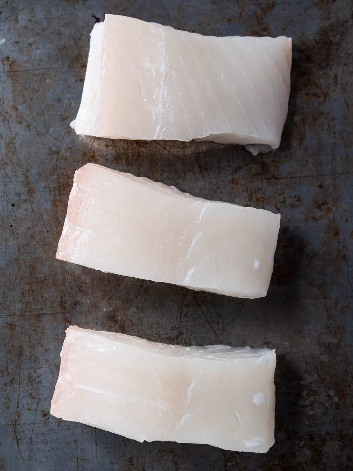 3 Raw halibut steaks on a sheet pan.