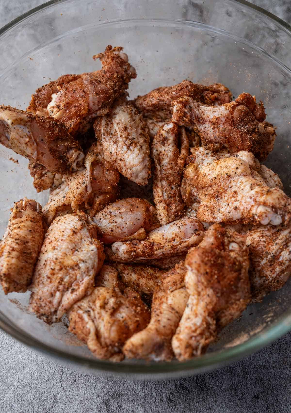 Raw chicken wings coated with dry rub in a large glass bowl