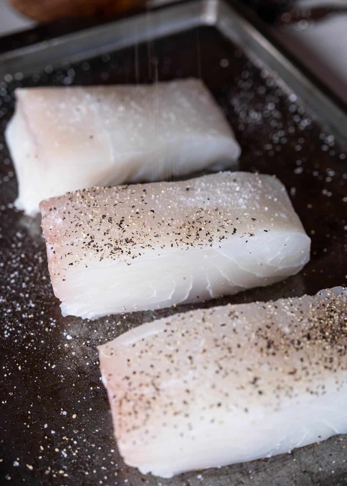 3 raw fish on a sheet tray and seasoned with kosher salt and black pepper.