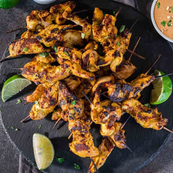 Grilled chicken satay skewers on a slate plate with peanut dipping sauce.