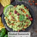 Smoked guacamole in a molcajete topped with bacon and cilantro surrounded by chips and greens.