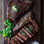 Two t-bone steaks on a cutting board, one sliced on a cutting board.