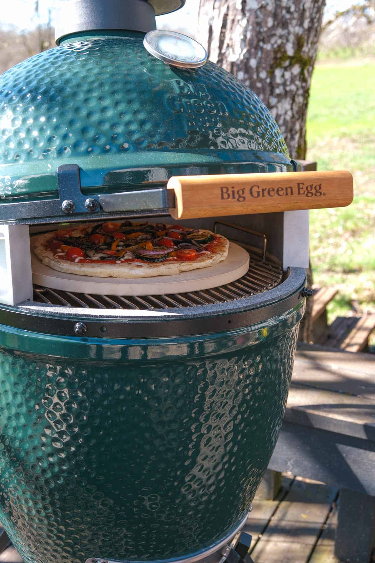 A pizza cooking on a pizza stone on a big green egg with the pizza wedge attachment.