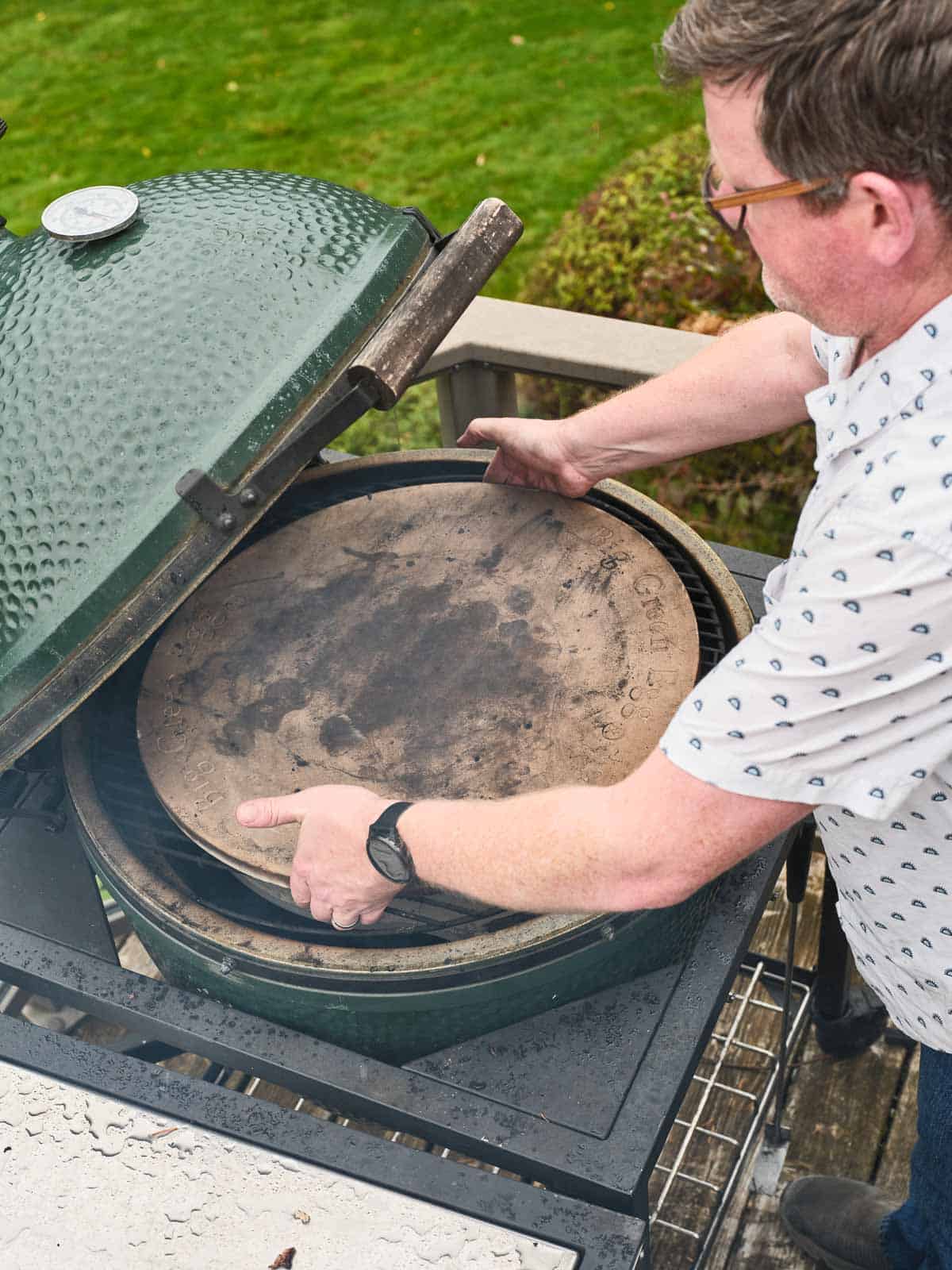 Placing a pizza stone on grill grates in a big green egg.