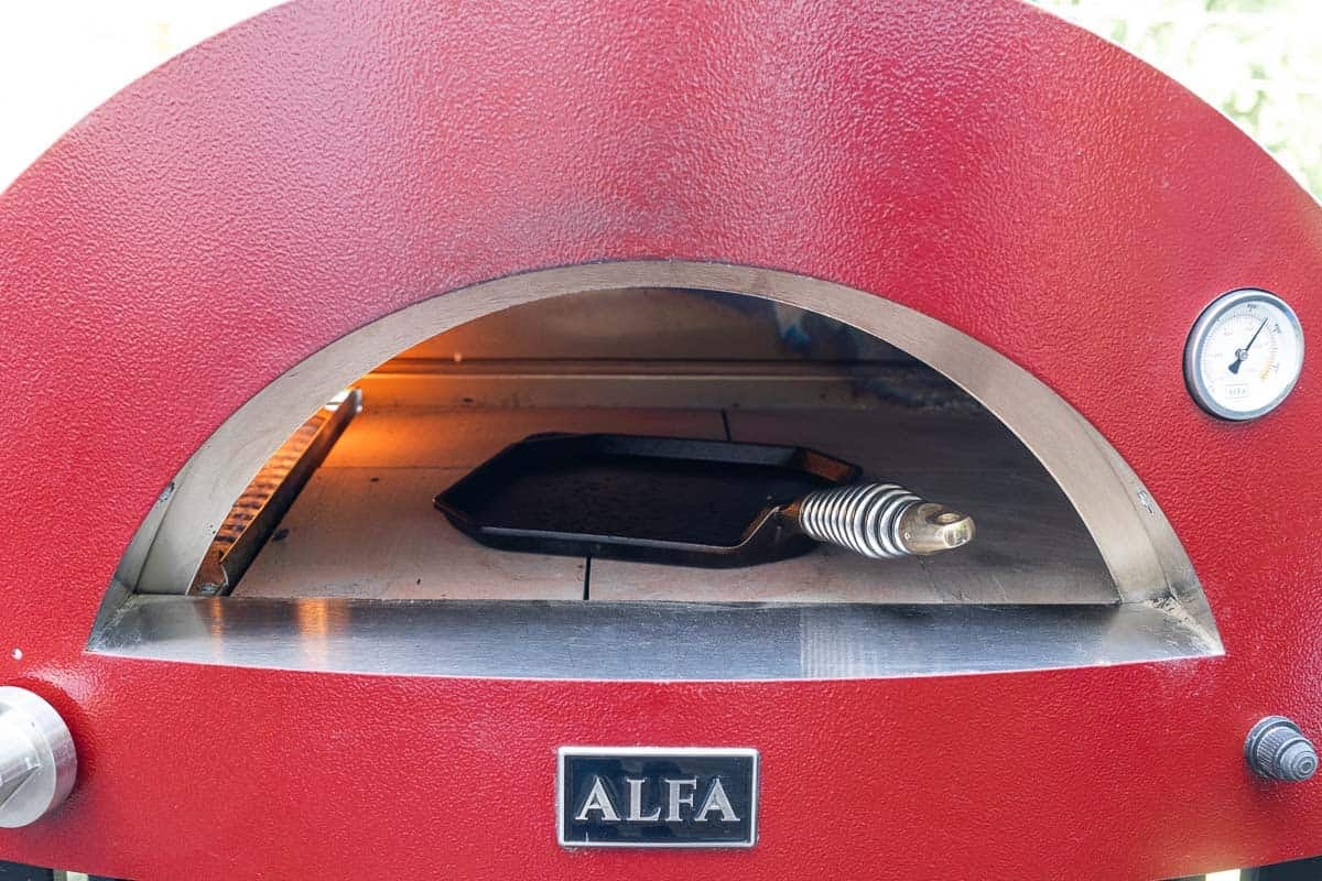 A cast iron pan preheating in a pizza oven before baking a steak.