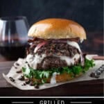 A wild mushroom burger piled with white cheddar cheese, mushrooms, and greens on a brioche bun on a cutting board.