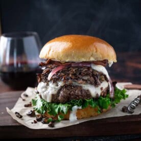 A Gourmet Burger topped with Sautéed Wild Mushrooms on a serving platter with a glass of red wine.