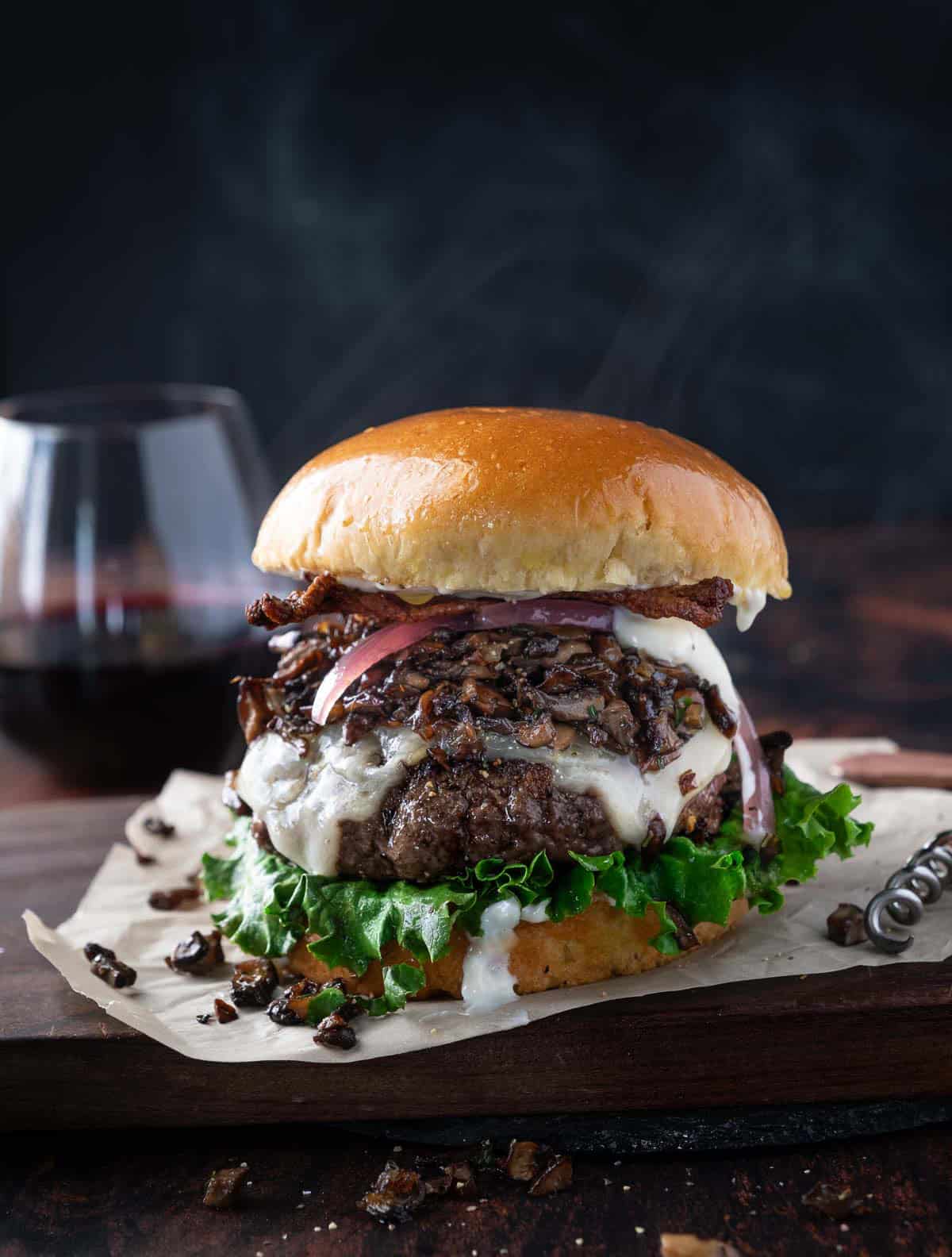 A Gourmet Burger topped with Sautéed Wild Mushrooms on a serving platter with a glass of red wine.