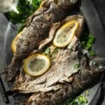 Three stuffed and grilled trout on a large serving platter, one is open to the viewer with a glass of wine.