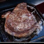 A ribeye steak on a cast iron pan after coming out of a pizza oven with a sear.
