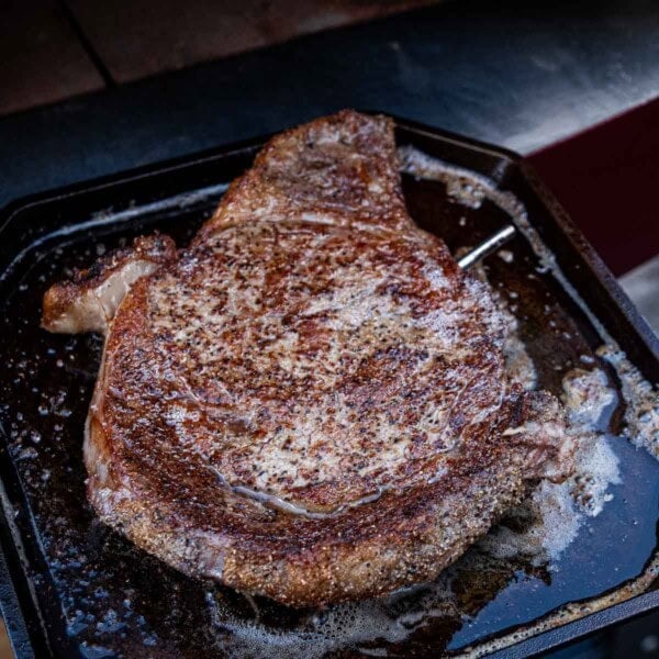 A steak on a cast iron griddle pan after being removed from the pizza oven.