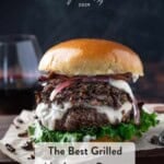 A wild mushroom burger piled with white cheddar cheese, mushrooms, and greens on a brioche bun on a cutting board.