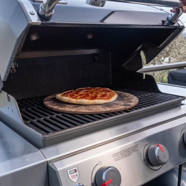 A pizza stone on a gas grill on the center grate.