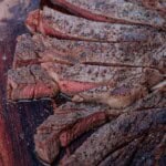 A ribeye steak sliced medium rare after being cooking in a pizza oven on cast iron.