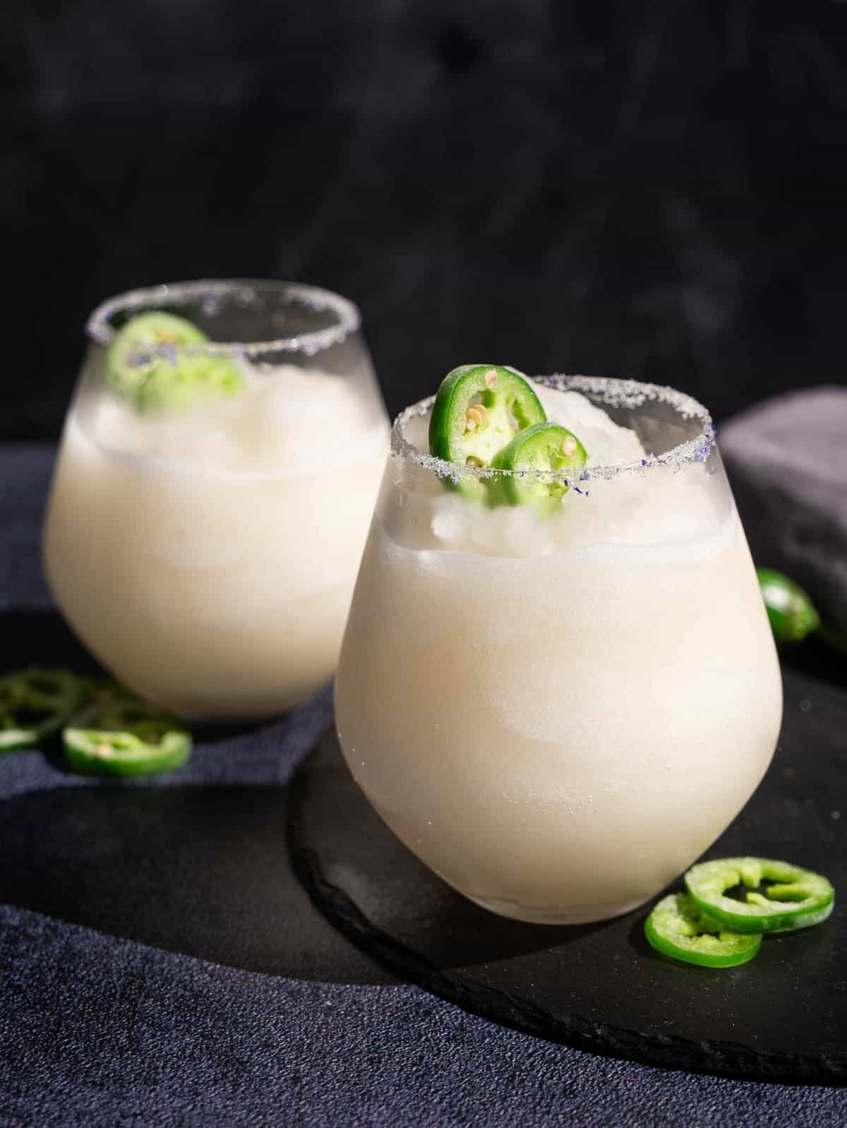 Two glasses of Jalapeño Sauvignon Blanc Slushie garnished with slices. of jalapenos. 