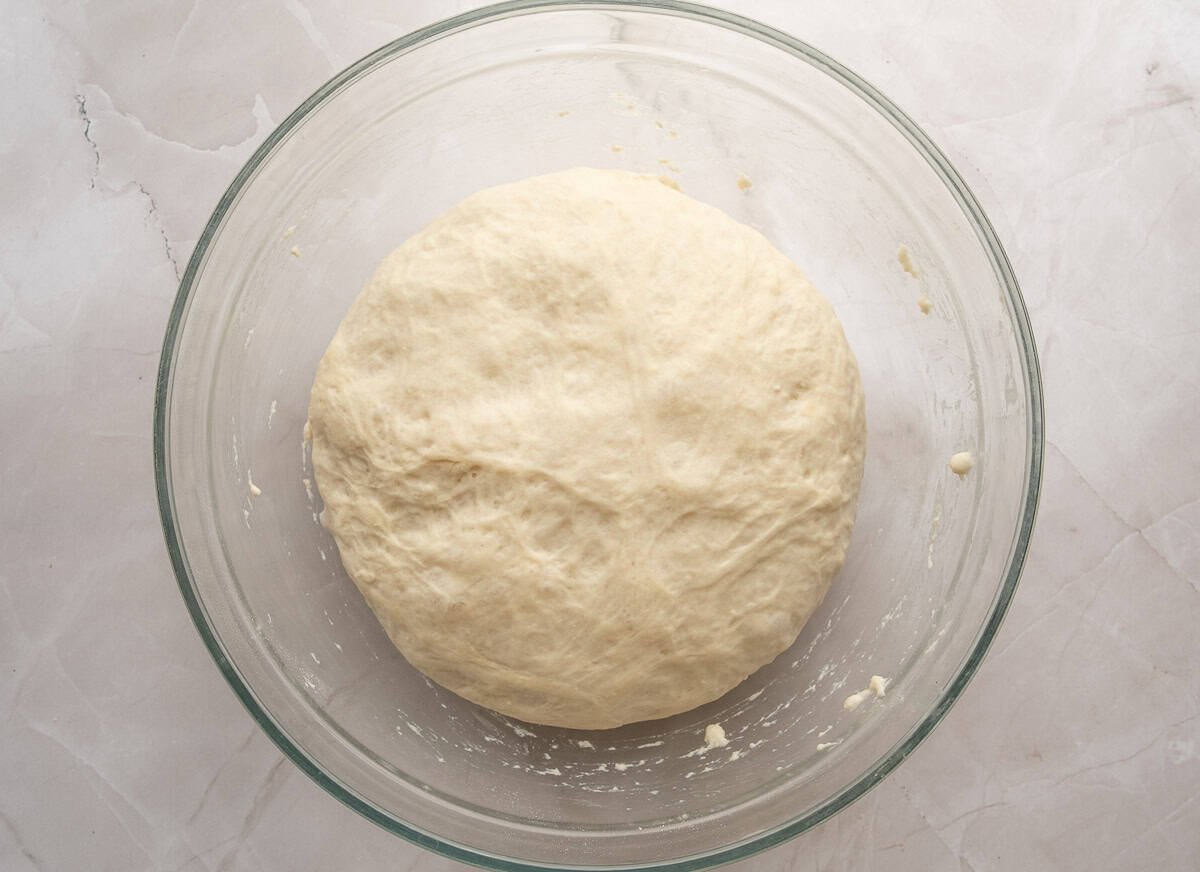 A pizza dough ball that has risen in a glass bowl.