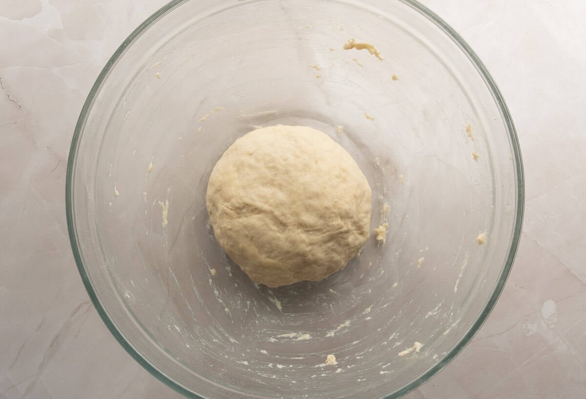 A pizza dough ball in a glass bowl before it's risen.
