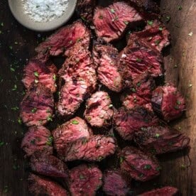 Slices of Grilled Hanger Steak on a cutting board with a small bowl of salt.