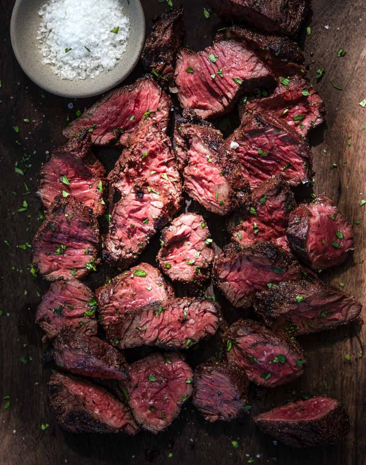 Slices of Grilled Hanger Steak on a cutting board with a small bowl of finishing salt.