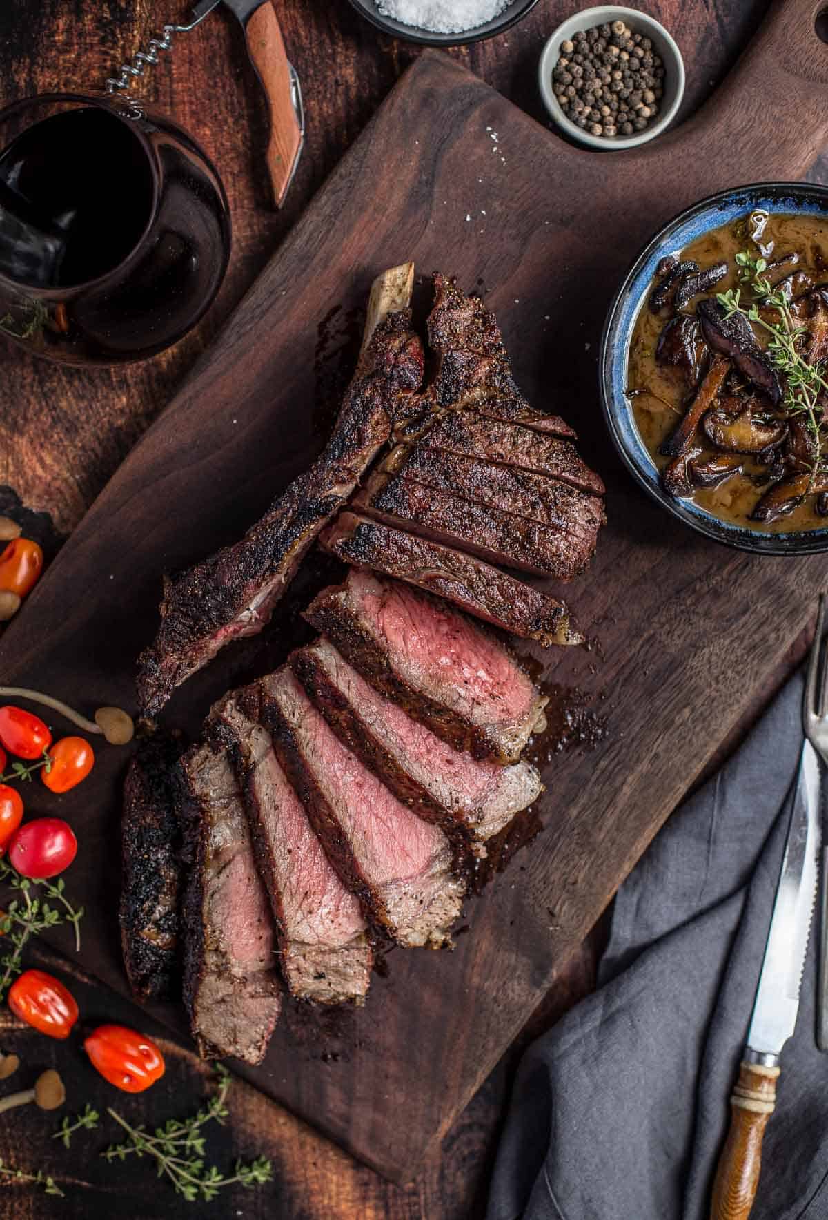 Grilled Cowboy Ribeye Steaks with a bowl of Red Wine Mushroom Sauce on a platter.