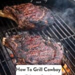 Two cowboy ribeye steaks on a grill over direct heat with the flame rising.
