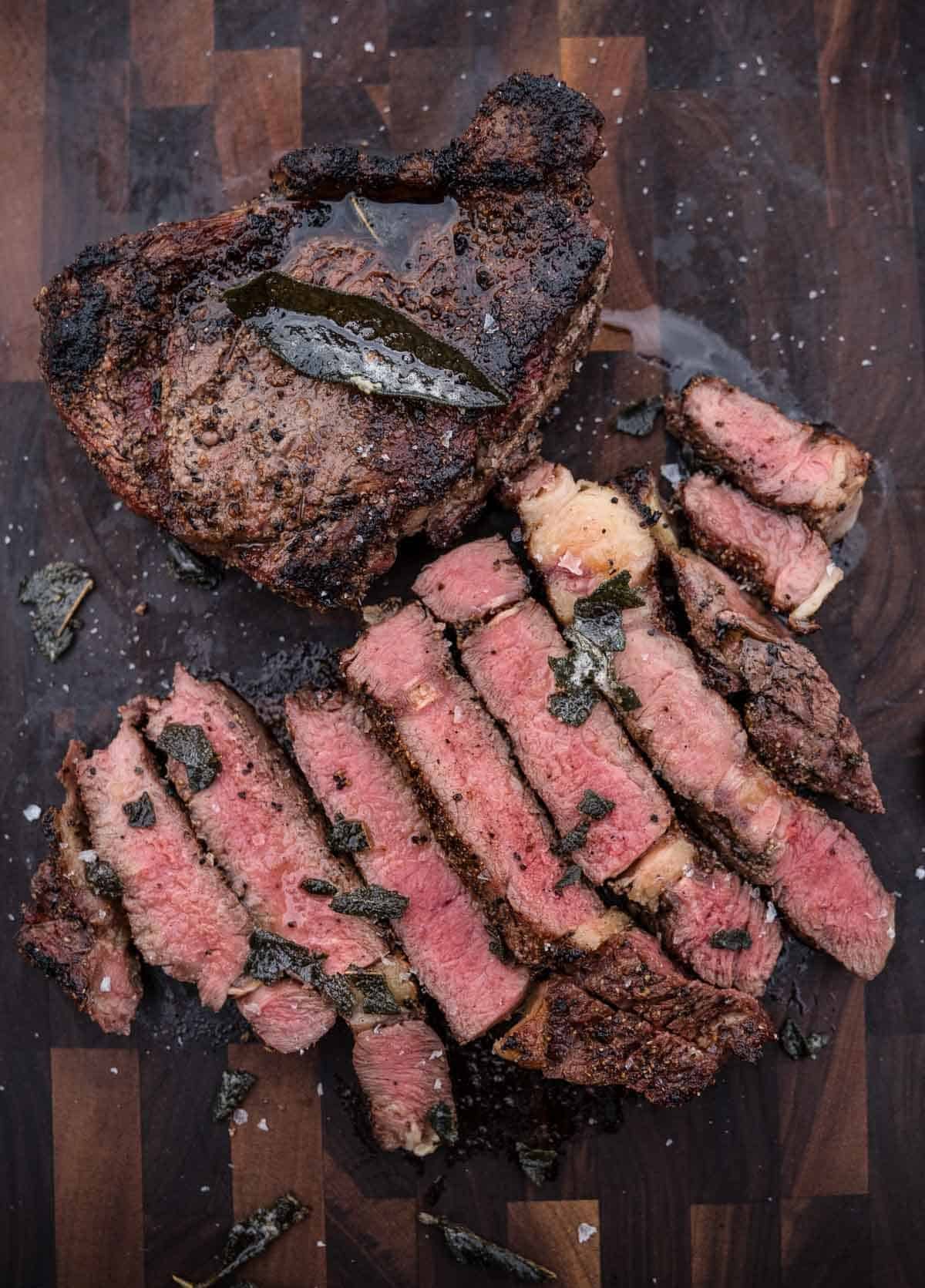 Two grilled bison steaks on a cutting board, one whole and one cut into slices.
