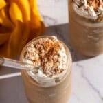Photo showing two pumpkin spice latte slushies topped with whipped cream on a marble table.
