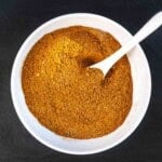 Moroccan spice blend in a white bowl with a spoon.