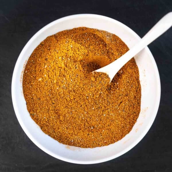Moroccan spice blend in a white bowl with a spoon.